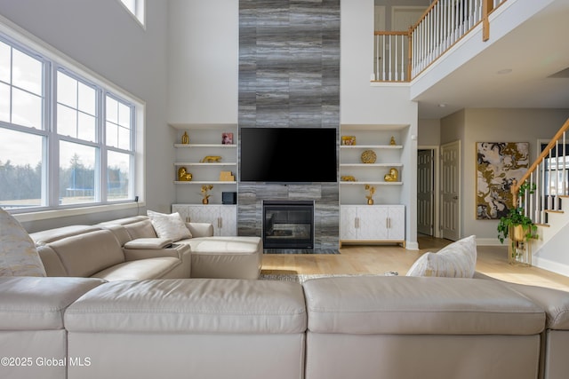 living area featuring built in features, wood finished floors, stairway, a high ceiling, and a fireplace