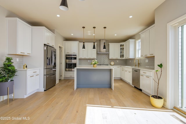 kitchen featuring light wood-style flooring, a kitchen island, appliances with stainless steel finishes, wall chimney exhaust hood, and light countertops