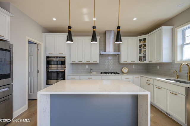 kitchen featuring stainless steel double oven, tasteful backsplash, a sink, and wall chimney range hood