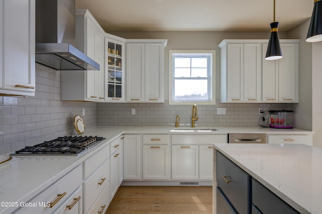 kitchen featuring visible vents, a sink, stainless steel gas stovetop, wall chimney exhaust hood, and white cabinets