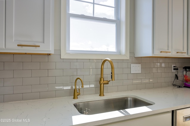 kitchen featuring a sink, backsplash, a wealth of natural light, and white cabinetry