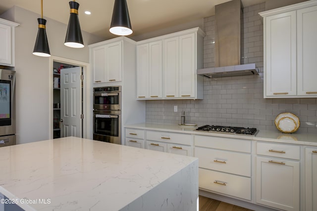 kitchen featuring light stone counters, decorative backsplash, stainless steel appliances, white cabinetry, and wall chimney exhaust hood