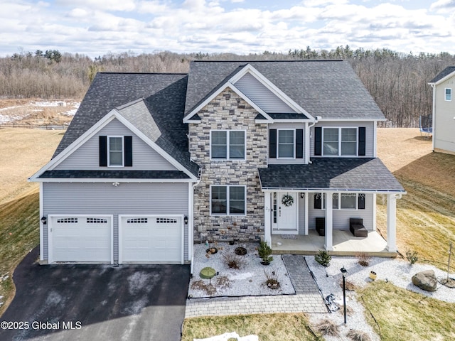 traditional-style home with a shingled roof, covered porch, a garage, stone siding, and driveway