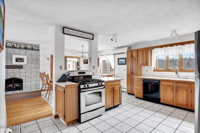 kitchen featuring stainless steel gas range oven, a wall mounted air conditioner, light countertops, black dishwasher, and a sink