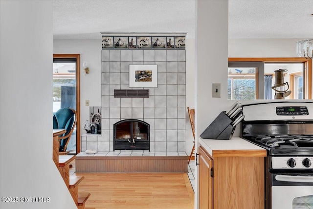 kitchen featuring a textured ceiling, light wood-style flooring, stainless steel gas range, and a tiled fireplace