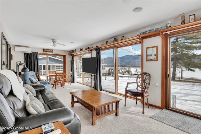 living area with a wall unit AC, a ceiling fan, light colored carpet, and baseboards