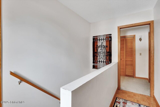 hallway featuring an upstairs landing, a textured ceiling, and baseboards