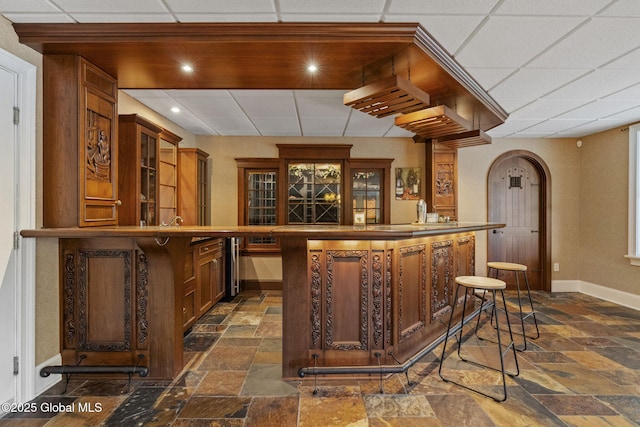 1014 Catherines Woods Dr, Niskayuna, NY 12309 - bar featuring baseboards, stone tile floors, a drop ceiling, and arched walkways