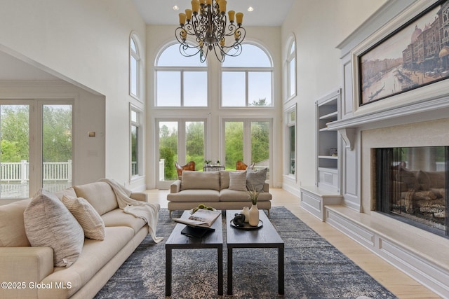 1014 Catherines Woods Dr, Niskayuna, NY 12309 - living room featuring light wood-type flooring, a towering ceiling, built in shelves, a chandelier, and a high end fireplace