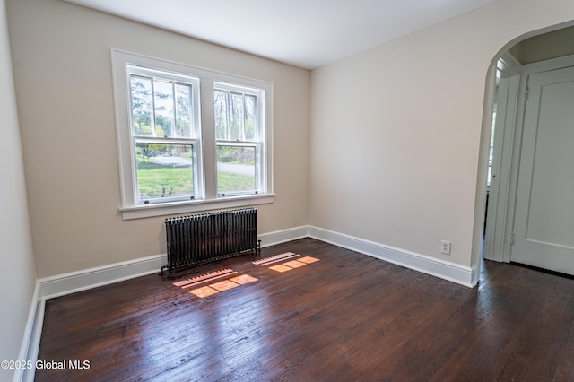 unfurnished room featuring baseboards, arched walkways, radiator, and dark wood-style flooring