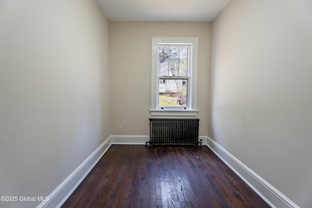 spare room featuring radiator, baseboards, and dark wood-type flooring