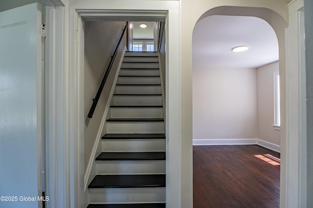 stairs with plenty of natural light, arched walkways, baseboards, and wood finished floors