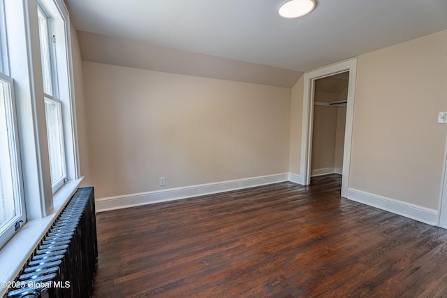 unfurnished bedroom with baseboards, radiator, dark wood-style flooring, and vaulted ceiling
