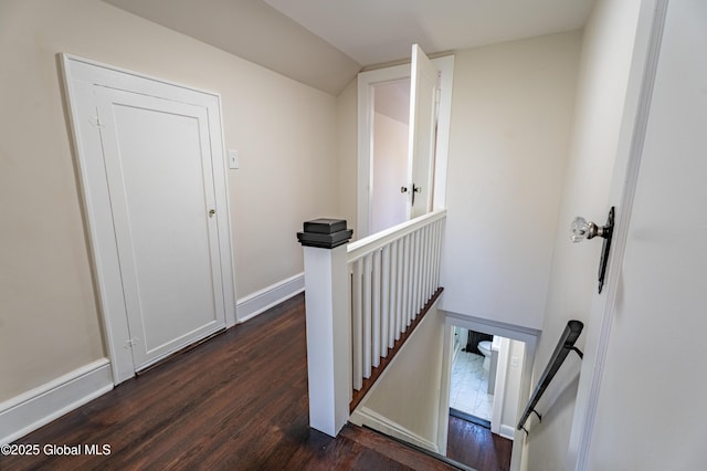 hall with baseboards, vaulted ceiling, dark wood-style floors, and an upstairs landing