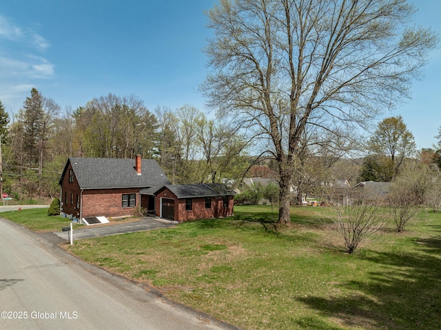 view of front of house featuring an attached garage, brick siding, a front yard, a chimney, and driveway