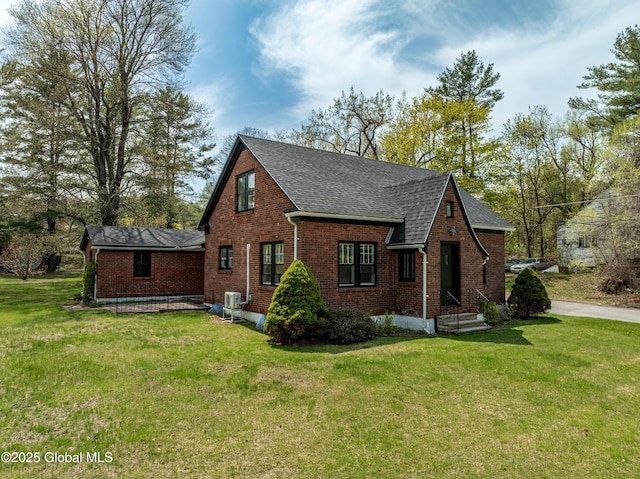 view of front of property with a shingled roof, a front yard, and brick siding