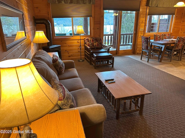 carpeted living area with a wood stove, wooden walls, and a wealth of natural light