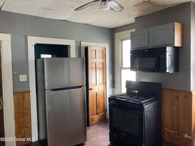 kitchen with black appliances, wood finished floors, a ceiling fan, and a paneled ceiling