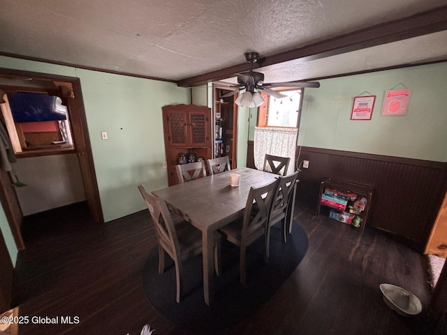 dining space featuring wooden walls, a wainscoted wall, ceiling fan, dark wood-type flooring, and a textured ceiling