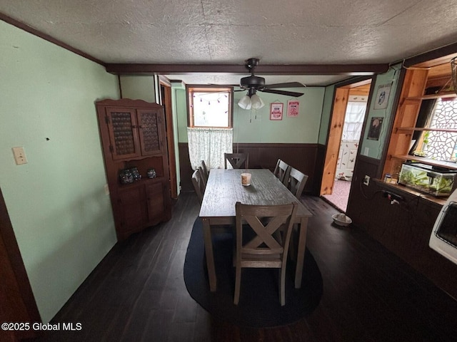 dining space with a wainscoted wall, a ceiling fan, a textured ceiling, wooden walls, and dark wood-style flooring