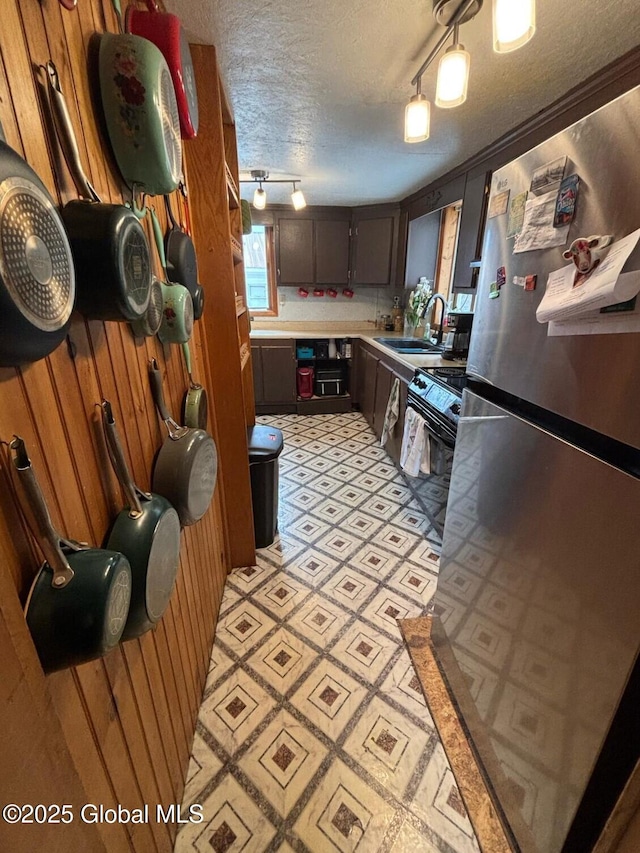 kitchen featuring electric range, a sink, a textured ceiling, freestanding refrigerator, and light countertops