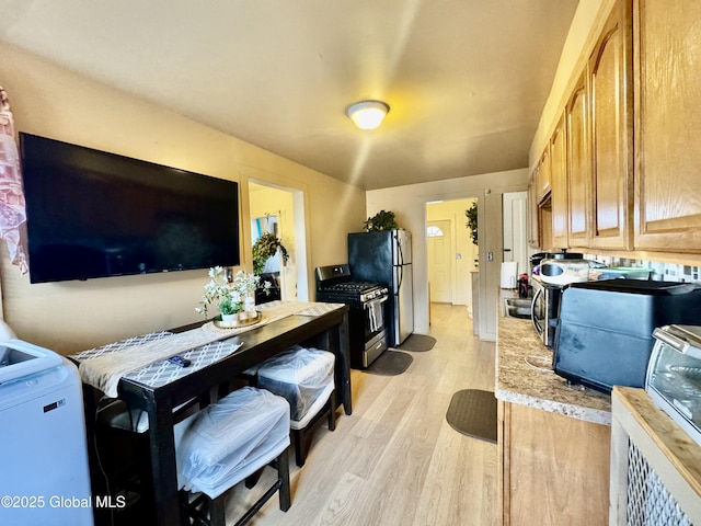 kitchen with stainless steel gas range oven, light wood-style floors, and freestanding refrigerator