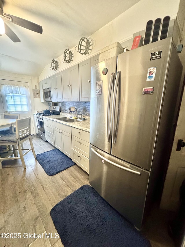 kitchen featuring light wood finished floors, backsplash, ceiling fan, stainless steel appliances, and a sink