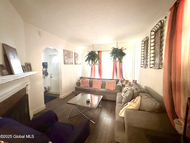 living area featuring arched walkways, a fireplace, baseboards, and wood finished floors
