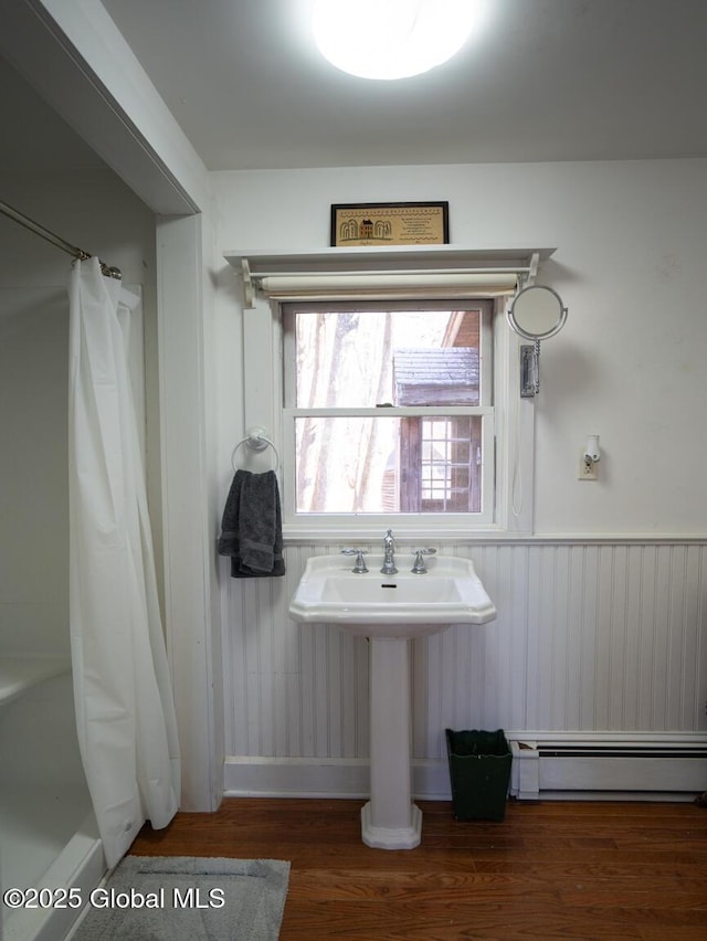 bathroom with wood finished floors, a baseboard radiator, wainscoting, a shower with curtain, and baseboards