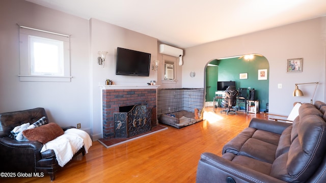 living room with arched walkways, a wall unit AC, light wood finished floors, and a fireplace