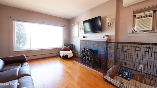 living area featuring a fireplace, baseboard heating, light wood finished floors, and a wall mounted air conditioner