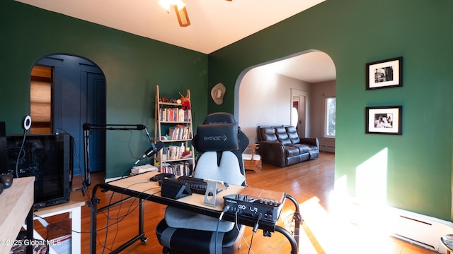 office with arched walkways, a baseboard heating unit, ceiling fan, and wood finished floors