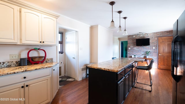 kitchen featuring freestanding refrigerator, wood finished floors, brick wall, a breakfast bar area, and decorative light fixtures