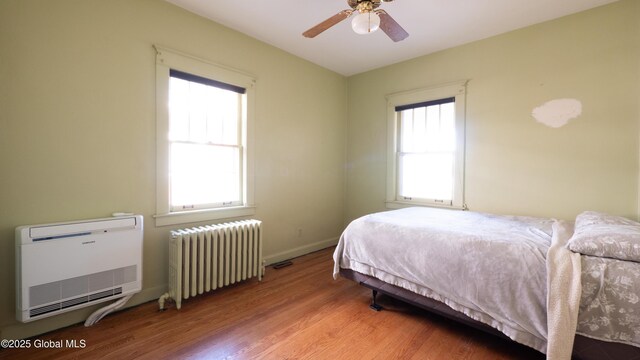 bedroom with ceiling fan, wood finished floors, baseboards, radiator heating unit, and heating unit