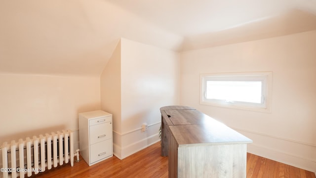 unfurnished office featuring baseboards, vaulted ceiling, light wood finished floors, and radiator
