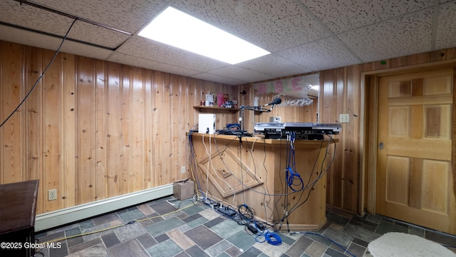 bar with a paneled ceiling, wooden walls, stone finish floor, and baseboard heating