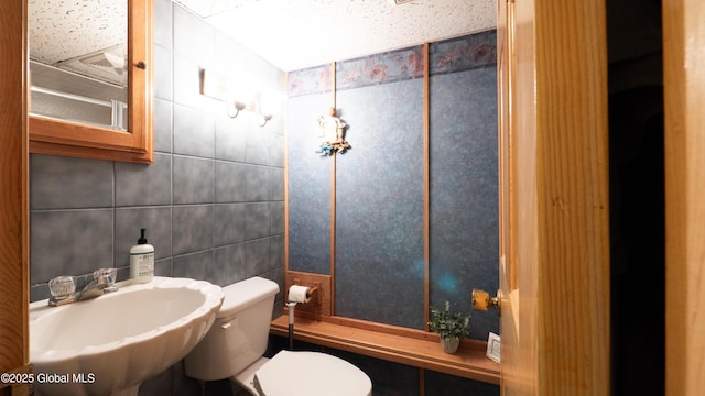 half bath with toilet, tile walls, and a sink