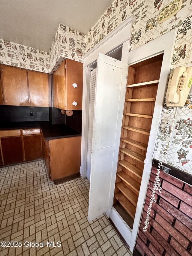 11 Middlesex Rd, East Greenbush, NY 12061 - kitchen with brown cabinetry, wallpapered walls, and brick floor