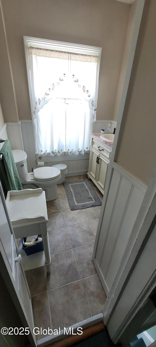755 County Route 7, Schodack, NY 12063 - bathroom featuring tile patterned floors, a wainscoted wall, toilet, a decorative wall, and vanity