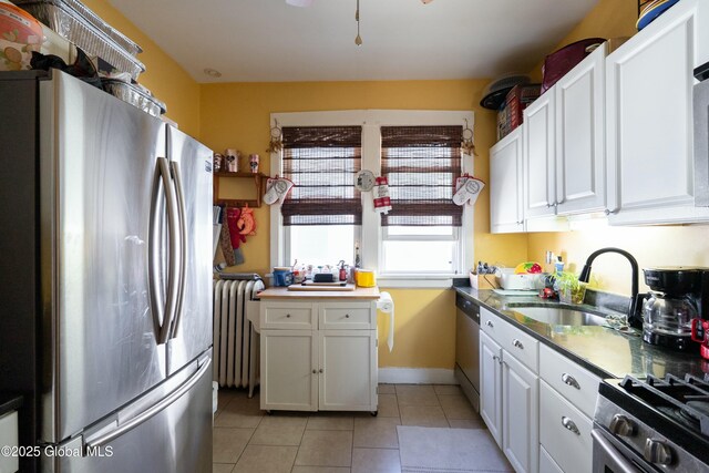 kitchen featuring radiator, light tile patterned flooring, a sink, stainless steel appliances, and white cabinets