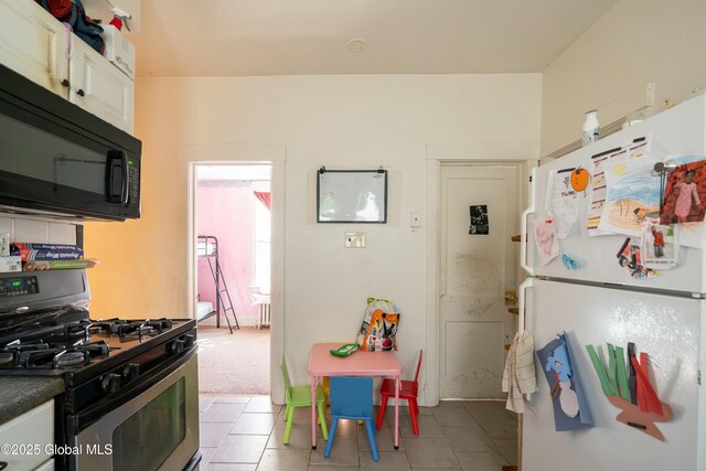 kitchen with dark countertops, freestanding refrigerator, black microwave, light tile patterned floors, and stainless steel gas range