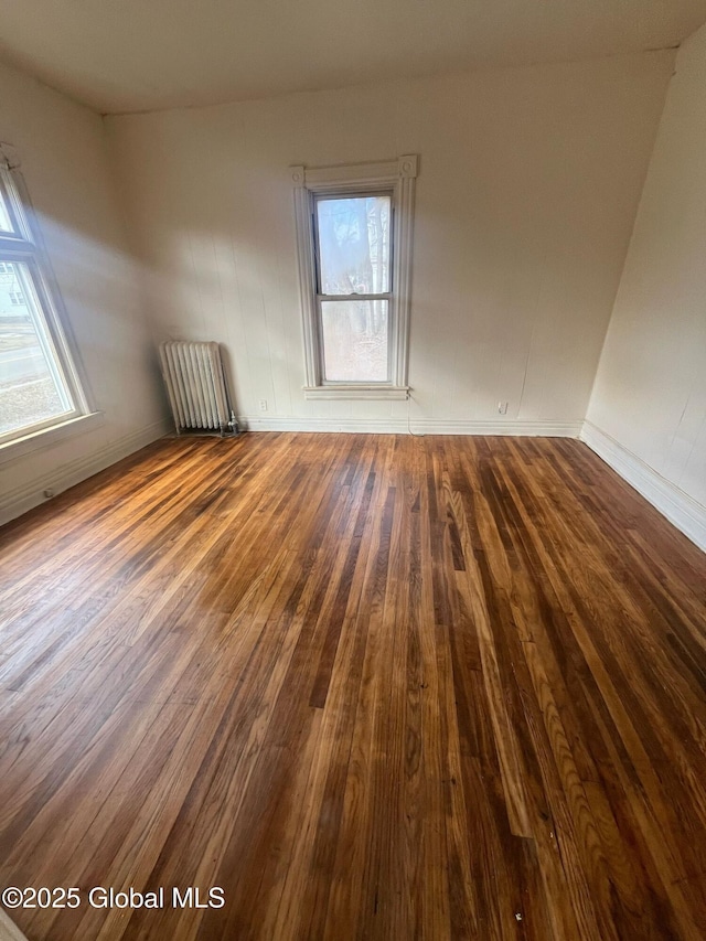spare room with baseboards, dark wood finished floors, and radiator heating unit