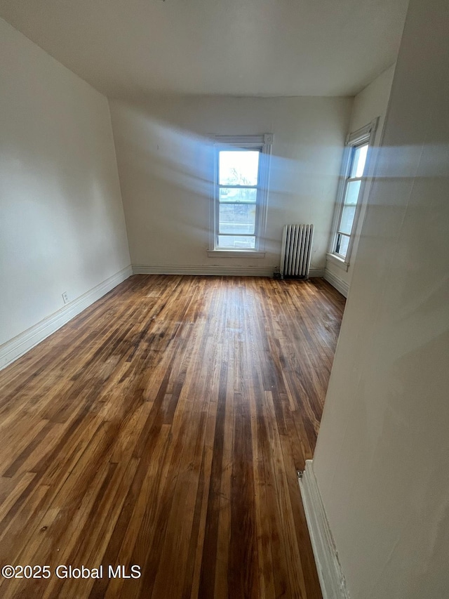spare room featuring baseboards, radiator heating unit, and hardwood / wood-style flooring