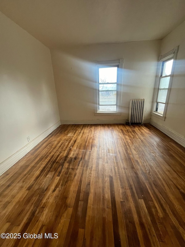 empty room featuring a wealth of natural light, dark wood finished floors, radiator heating unit, and baseboards