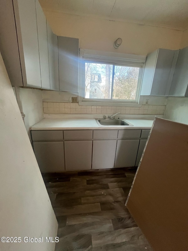 kitchen with a sink, dark wood-type flooring, white cabinets, light countertops, and tasteful backsplash