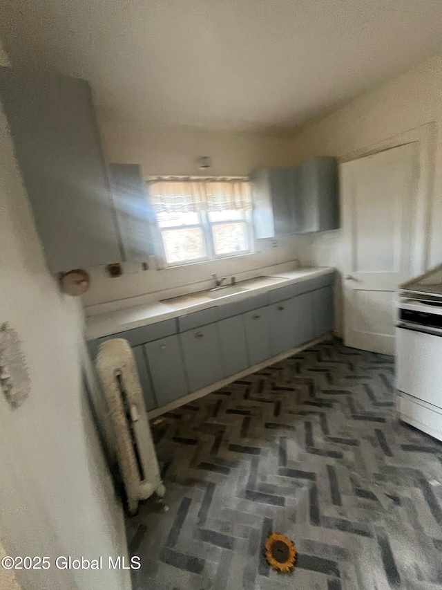 kitchen featuring stainless steel range with electric stovetop, light countertops, radiator heating unit, and a sink