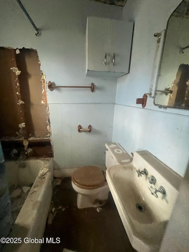 bathroom featuring toilet, a bathing tub, wainscoting, a shower, and a sink