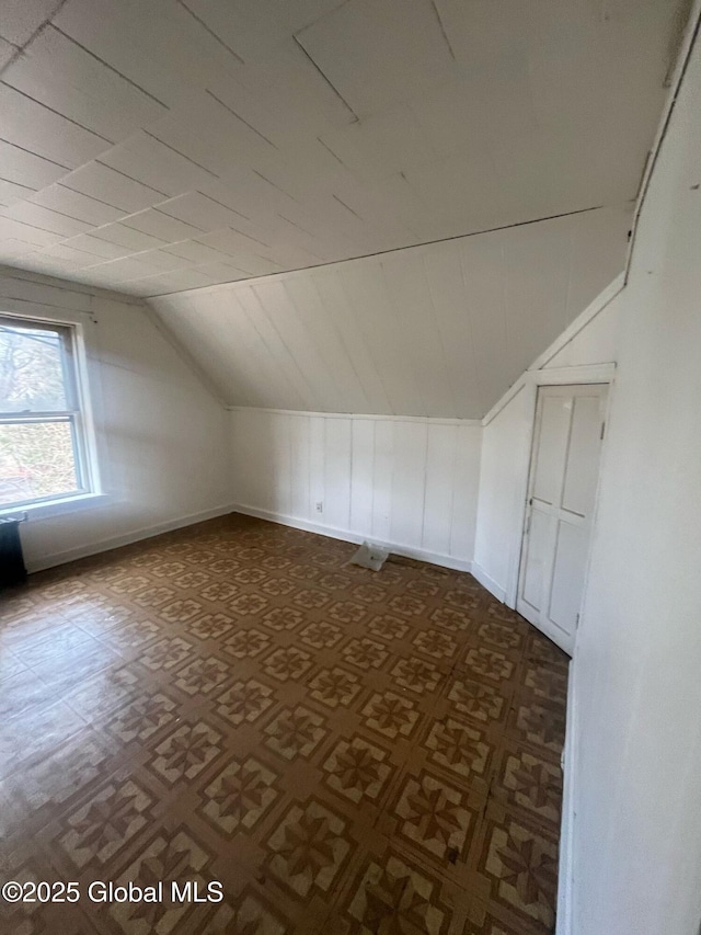 additional living space featuring baseboards, lofted ceiling, and dark floors