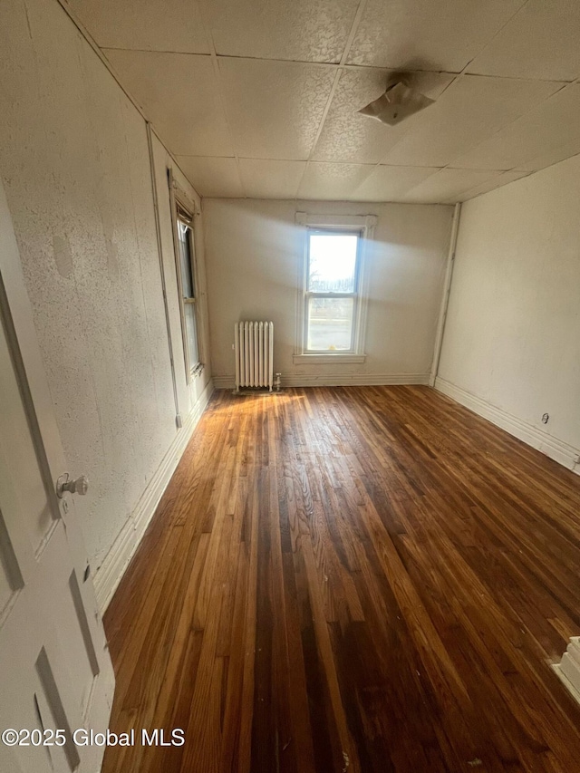 unfurnished room with baseboards, a paneled ceiling, radiator, and hardwood / wood-style flooring