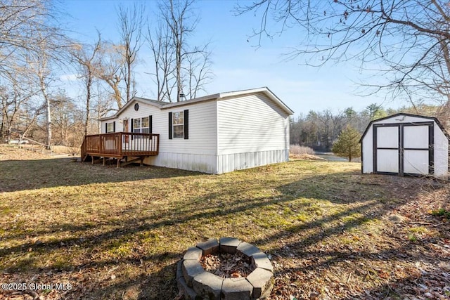 view of side of property featuring an outdoor structure, a deck, a storage shed, a fire pit, and a lawn